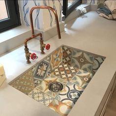 a sink in a bathroom with colorful tiles on the floor and walls behind it, next to a window