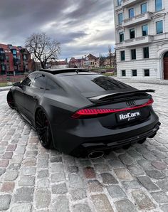 a black sports car parked in front of a tall building on a cobblestone street