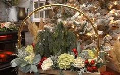 a basket filled with flowers and greenery next to a christmas tree in front of a fireplace