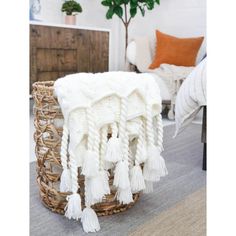 a white blanket sitting on top of a basket next to a plant in a living room