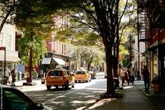 cars are driving down the street in front of shops and people walking on the sidewalk