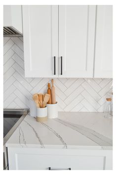 a kitchen with white cabinets and marble counter tops in the center is an oven, utensils, and cutting board