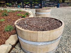 two wooden barrels sitting next to each other on top of gravel covered ground in front of a fence