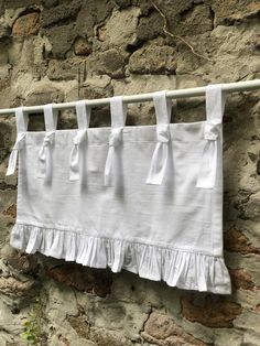 white ruffled curtains hanging on a clothesline against a stone wall with ivy growing in the foreground