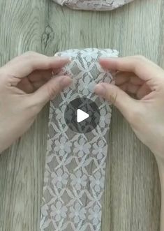 two hands holding up a piece of lace on top of a wooden table next to another person's hand