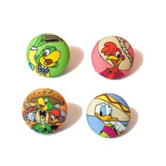 four pinback buttons with cartoon characters on them, all in different colors and sizes