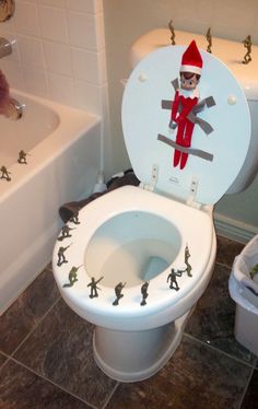 an elf on the lid of a toilet in a bathroom with toy soldiers around it