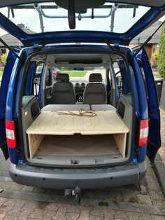 the back end of a blue van with an open trunk and wooden table in it