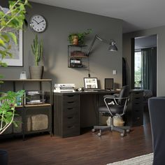 an office with a desk, chair and clock on the wall next to a potted plant