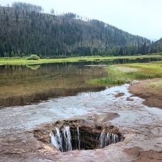 a hole in the ground with water coming out of it and mountains in the background