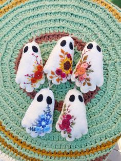 four little white ghost decorations on a crocheted place mat with flowers and leaves