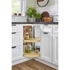 a kitchen with white cupboards and wooden flooring has a clock on the wall