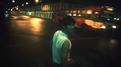 a man standing on the side of a road at night with a bus in the background