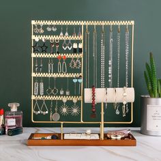 a gold jewelry rack with earrings and other accessories on it next to a potted plant