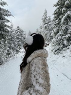 a woman is walking through the snow with her back to the camera and trees in the background