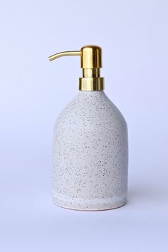 a white and gold colored soap dispenser on a white surface with a golden top