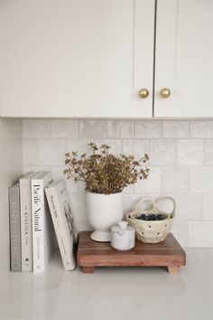 a kitchen counter with some books and a bowl on it next to a vase filled with flowers