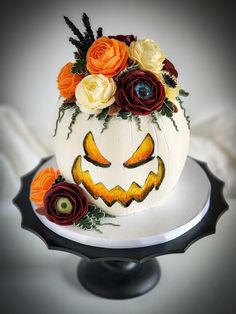 a decorated pumpkin sitting on top of a white cake with orange and red flowers around it