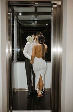 a man and woman are standing in an elevator, one is wearing a white dress