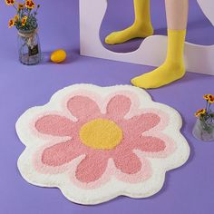 a person standing next to a flower rug and vase with flowers in it on a purple surface