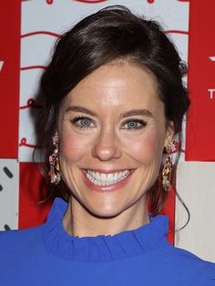 a smiling woman in a blue dress with earrings on her head and hair pulled back