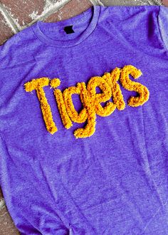 Make a bold statement with the Tigers Chenille Applique' T-shirt in Purple .  This super-soft and lightweight t-shirt offers a classic/unisex fit. Crafted with a blend of 65% polyester and 35% cotton, this tee ensures both durability and comfort, designed to withstand the test of time.   The Tigers Chenille Applique' T-shir t is tailored for women who appreciate fashionable and comfortable shirts, available in sizes ranging from Small to 3x.    At Jimberlys , we deeply care about your satisfaction and take pride in offering high-quality apparel that meets your unique fashion needs.   This item pairs well with ... Risen Jeans  - Yellowbox Footwear  -   Crossbody Bags  - All Chenille T-Shirts   Can you wash & dry the Tigers Chenille Applique' T-shirt ? Absolutely! The Tigers Chenille Appliqu Sweater With Chenille Letters, Disney Chenille Patch Sweatshirt, Chenille Letter Shirts, Chenille Sweatshirt, Risen Jeans, Charles River Rain Jacket, Chenille Applique, Menswear Women, Comfortable Shirts