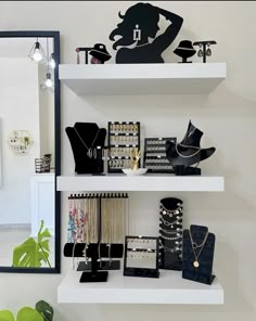 a white shelf topped with lots of different types of jewelry next to a mirror and potted plant