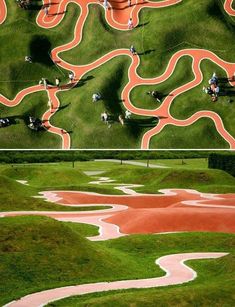 an aerial view of a green field with red and white markings on the grass as well as people walking down it