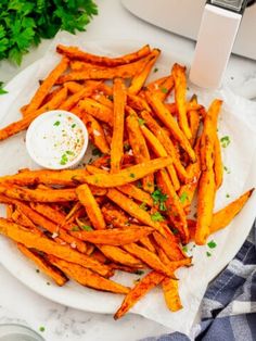 baked sweet potato fries on a white plate with parsley in the background and an air fryer to the side