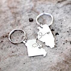 two metal key chains with the shape of illinois and heart shaped dots on them sitting on a stone surface