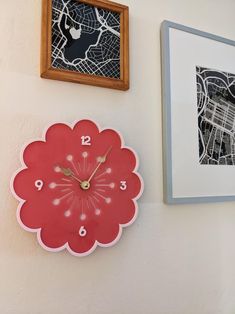 a red clock mounted to the side of a wall next to two framed pictures on a wall