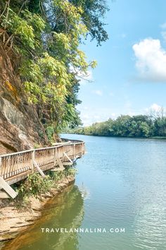 a wooden bridge over a body of water near a cliff and tree covered hill side