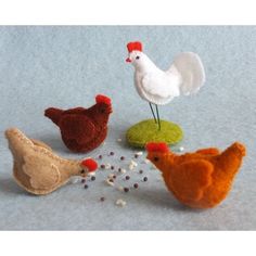 four different types of felt chickens on a blue surface with food scattered around them and one chicken pecking at the ground