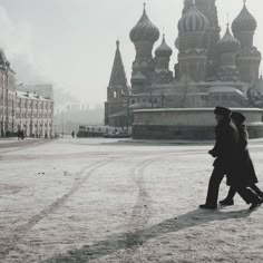 two people are walking in the snow near some buildings with spires on top of them