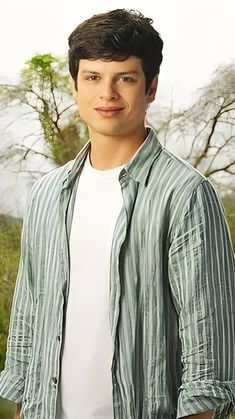 a young man standing in front of a green field with trees and grass behind him