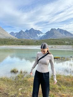 a woman standing on top of a grass covered field next to a body of water