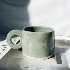 a green coffee cup sitting on top of a magazine next to a white sheet with black speckles