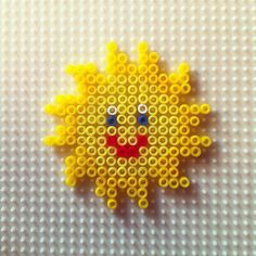 a yellow beaded sun with two small eyes on it's face, sitting on a white surface