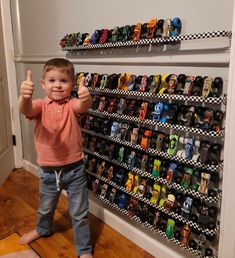 a young boy giving the thumbs up in front of a display of cars and trucks