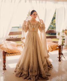 a woman in a wedding dress is standing near a bed with sheer drapes on the windowsill