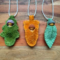 three leaf shaped ornaments hanging from strings on a wooden surface with two small figurines in the middle