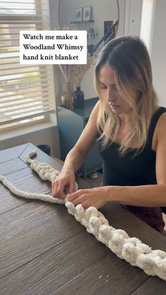 a woman is working with yarn on a wooden table in front of a window that reads, watch me make a woodland whimsy hand knit blanket