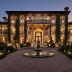 a large mansion with a fountain in front of it at night time, lit up by lights