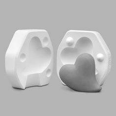 two white heart shaped vases sitting next to each other on a gray background,