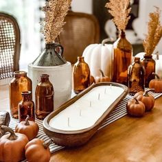 a table topped with bottles and pumpkins on top of a wooden table covered in candles