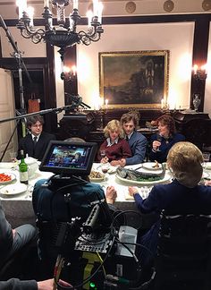 a group of people sitting around a table in front of a tv camera with food on it