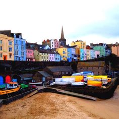 several boats are parked on the beach in front of some colorful buildings and sand dunes