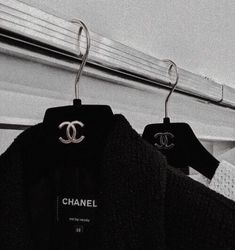 two black sweaters hanging on clothes racks in a closet, one with the word chanel written on it