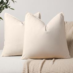 two white pillows sitting on top of a bed next to a plant in a vase