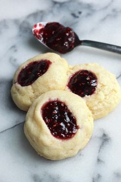 three cookies with jam on them sitting next to a spoon